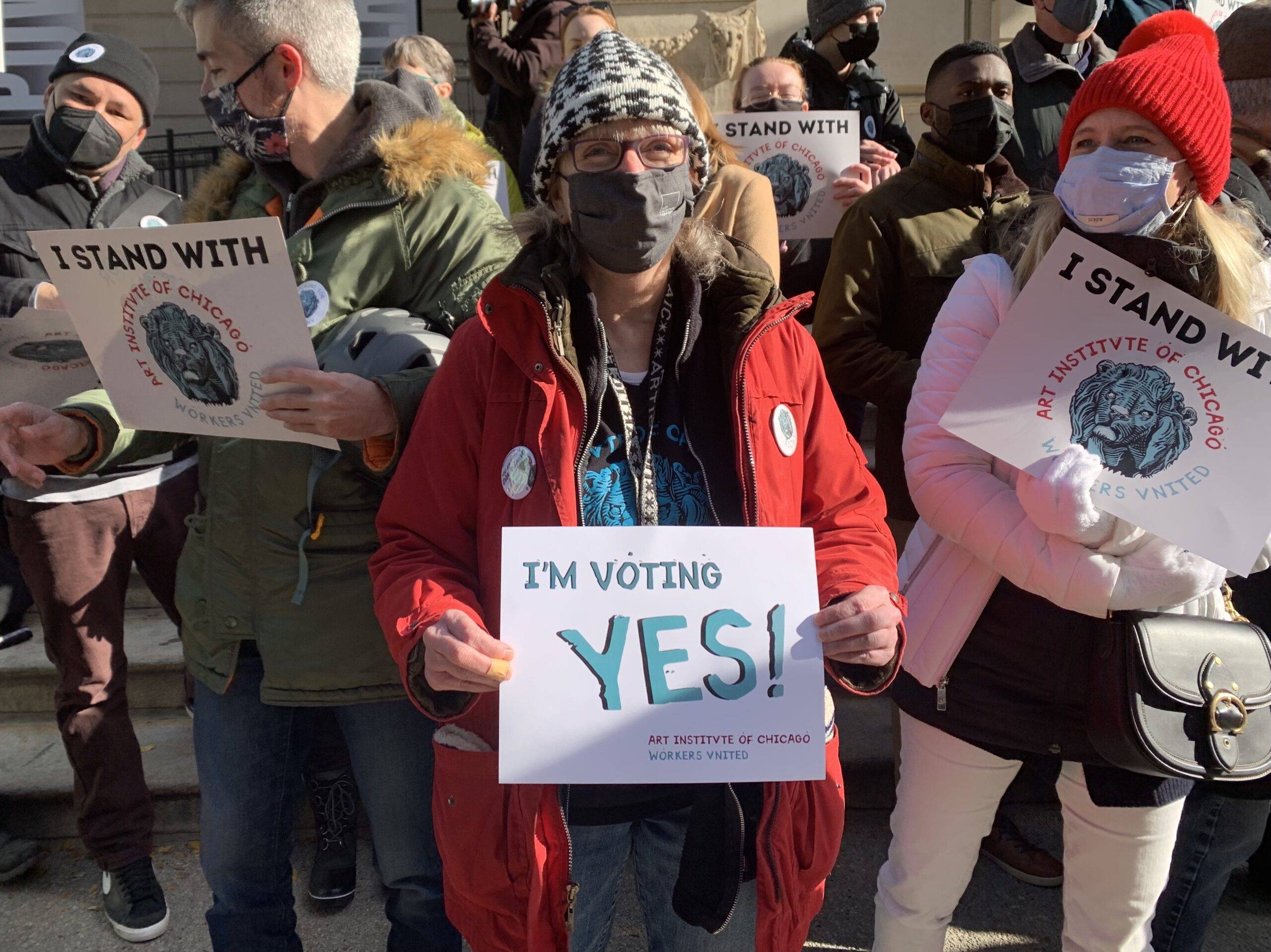 A woman in a red puffy jacket holds a sign which reads: "I'm voting Yes."