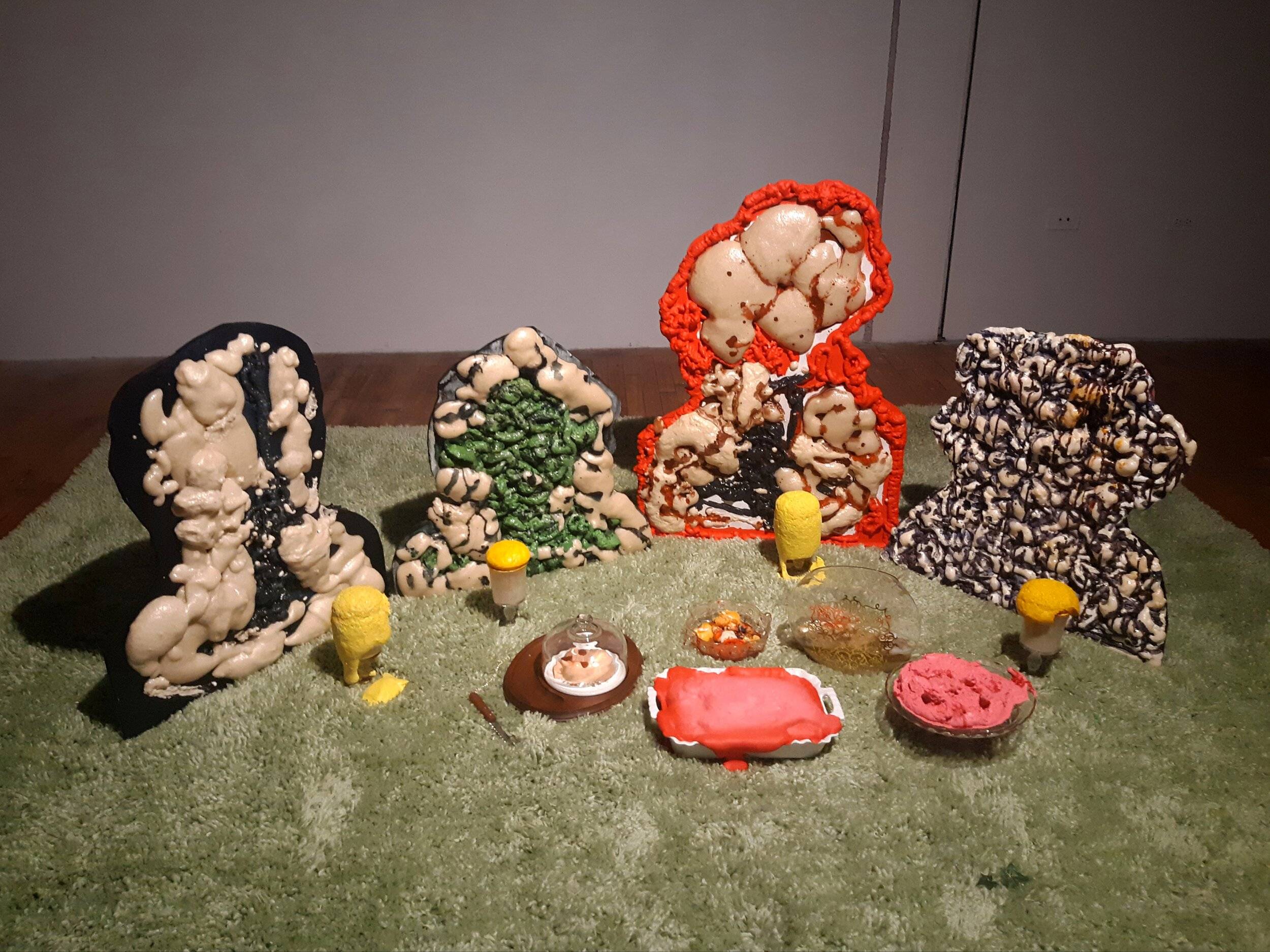 Four lumpy figures sit around an array of abstract drink glasses and foods.