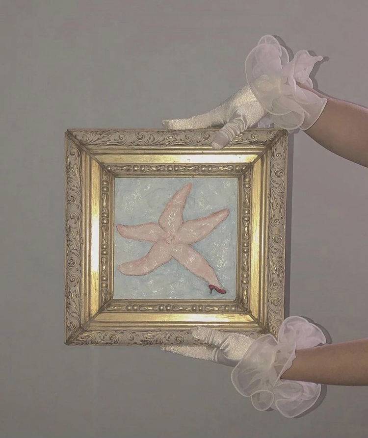 Two gloved hands hold a pastel-colored painting of a star fish wearing heeled shoes.