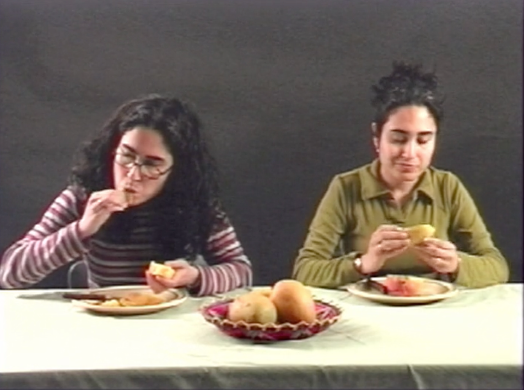 Two South Asian women sit next to each other eating mangoes.