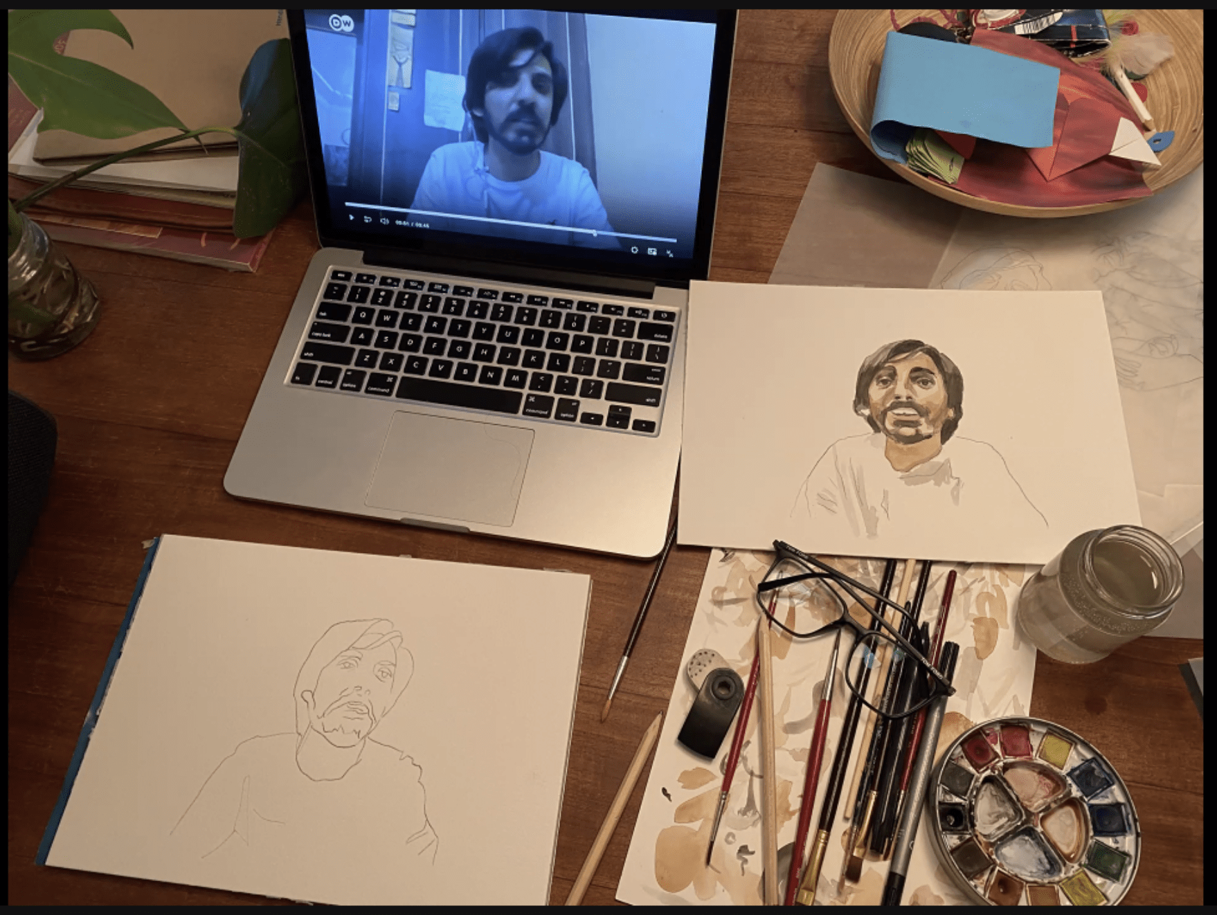 A laptop with a man's face next to a water color portrait of the same man's face.