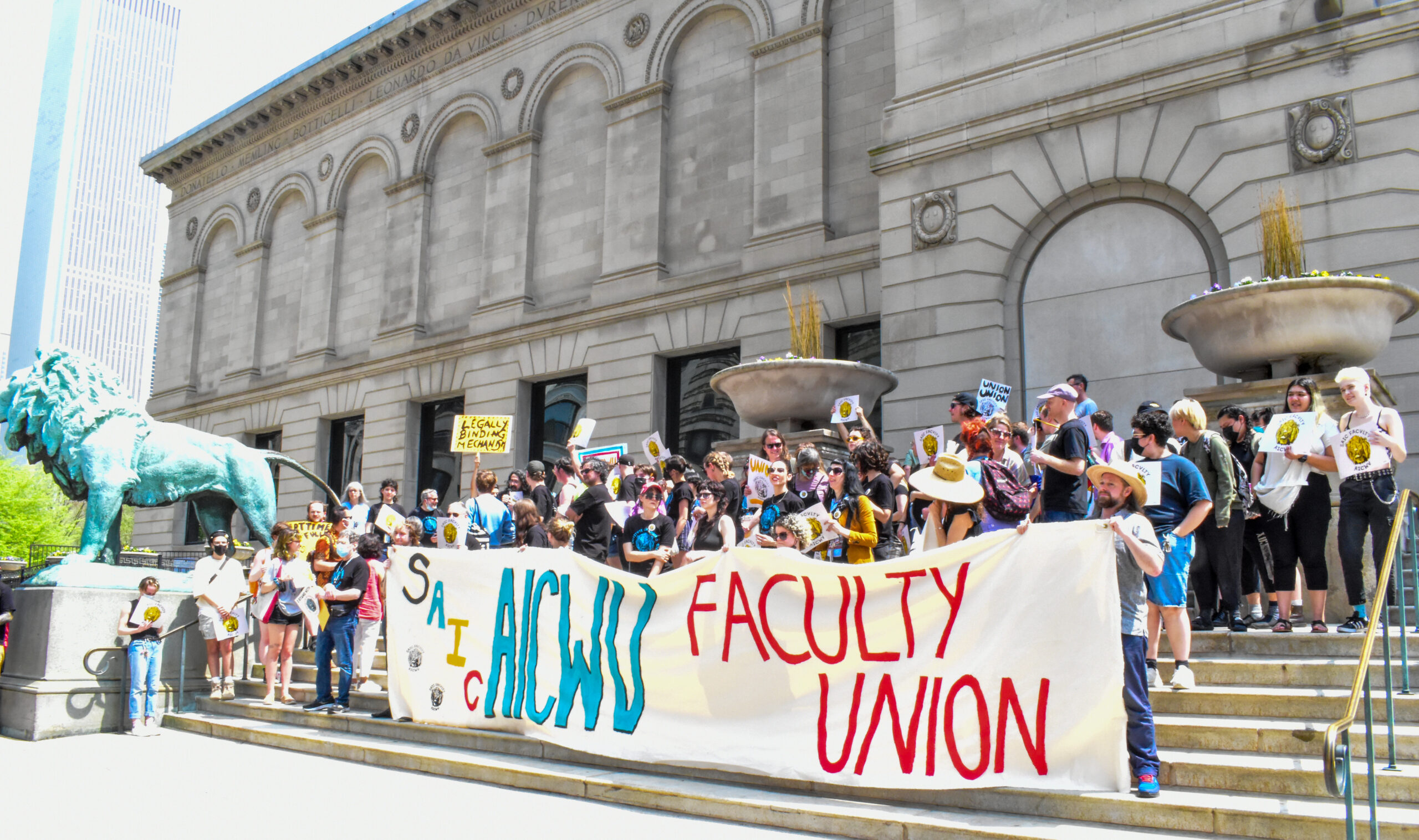 Dozens gather on the steps of the Art Institute with a banner that reads "SAIC AICWU Faculty Union."