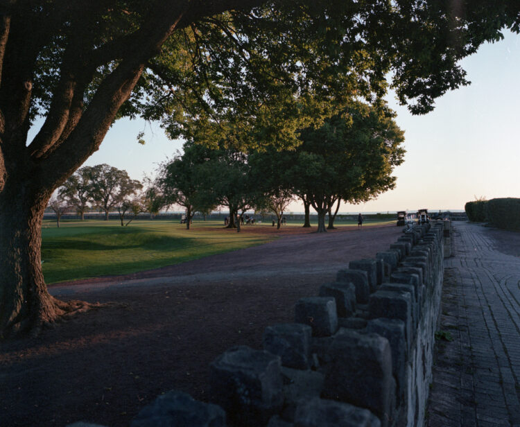 An early morning view of golfers getting ready to play, with a stone wall in the foreground.