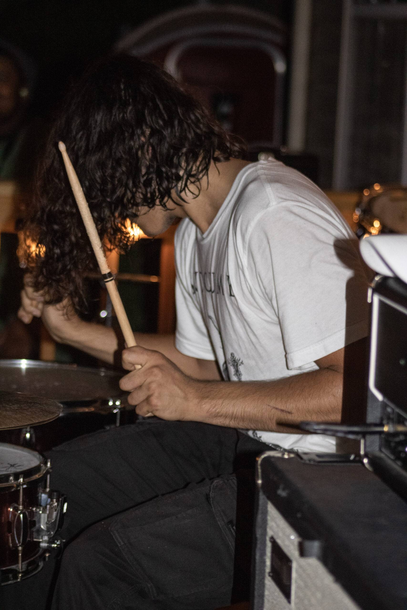A long-haired drummer works his way through a beat while performing.
