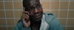 A distraught Black man with glasses holds a cell phone.