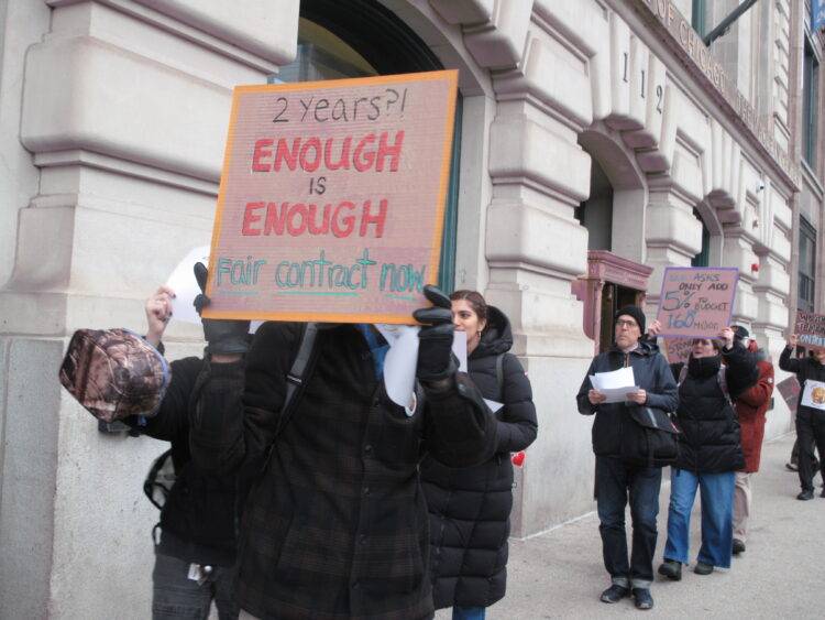 A protester at AICWU’s informational picket holds a sign that says “2 years?! ENOUGH is ENOUGH Fair contract now.”